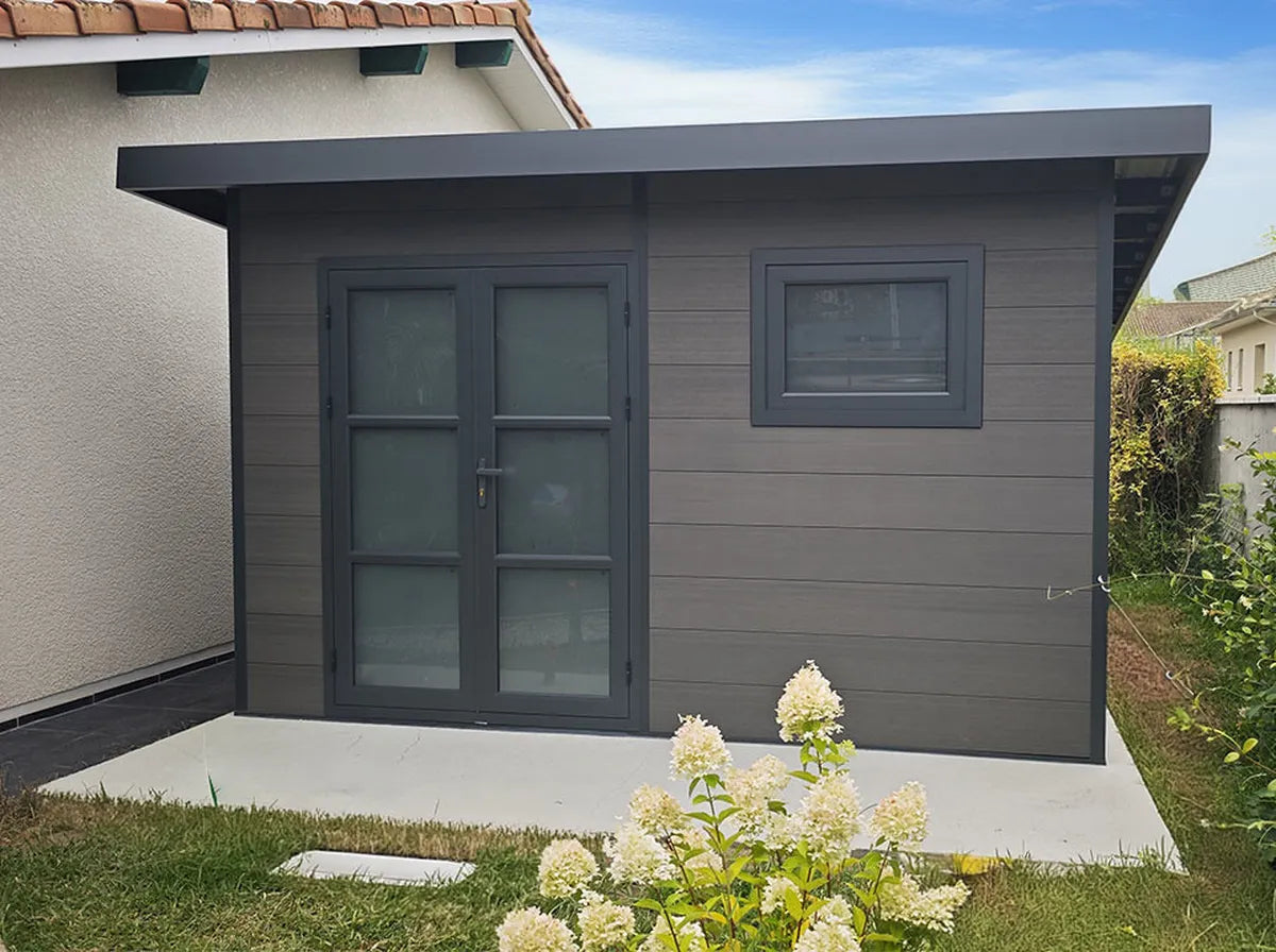 Abri composite gris avec fenêtre, installé chez un client contre la maison