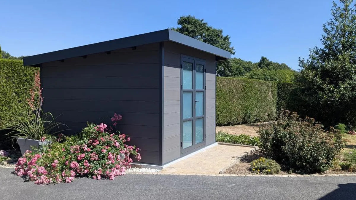 Abri composite gris installé chez un client, massif de fleurs devant