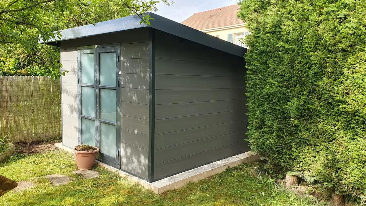 Abri composite gris clair installé chez un client contre une haie
