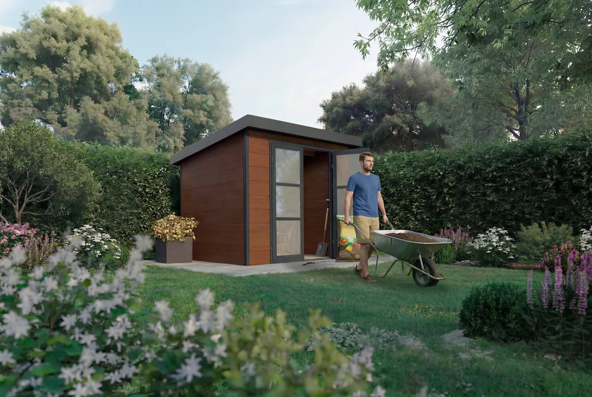Abri composite Alma 5 m² brun dans un jardin, homme avec une brouette