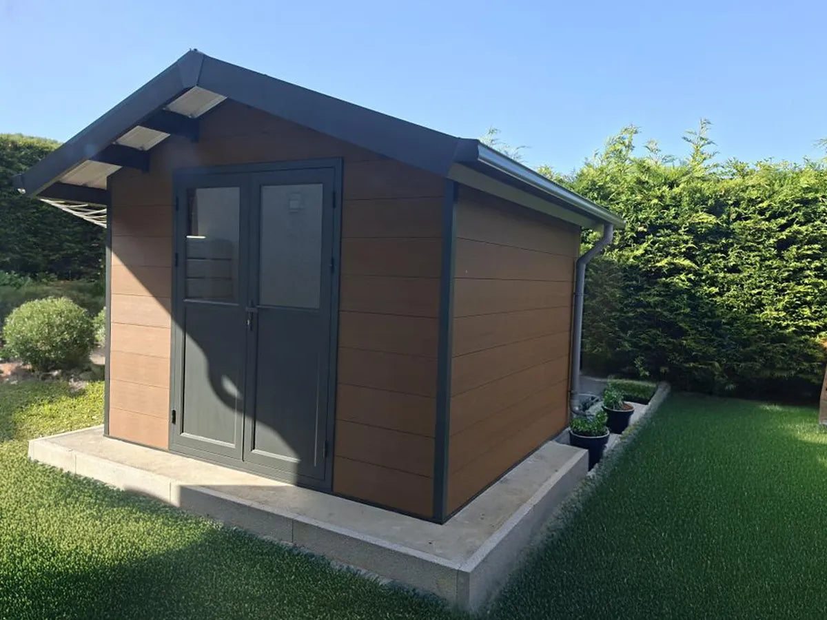 Abri composite Isora brun installé chez un client, au soleil couchant